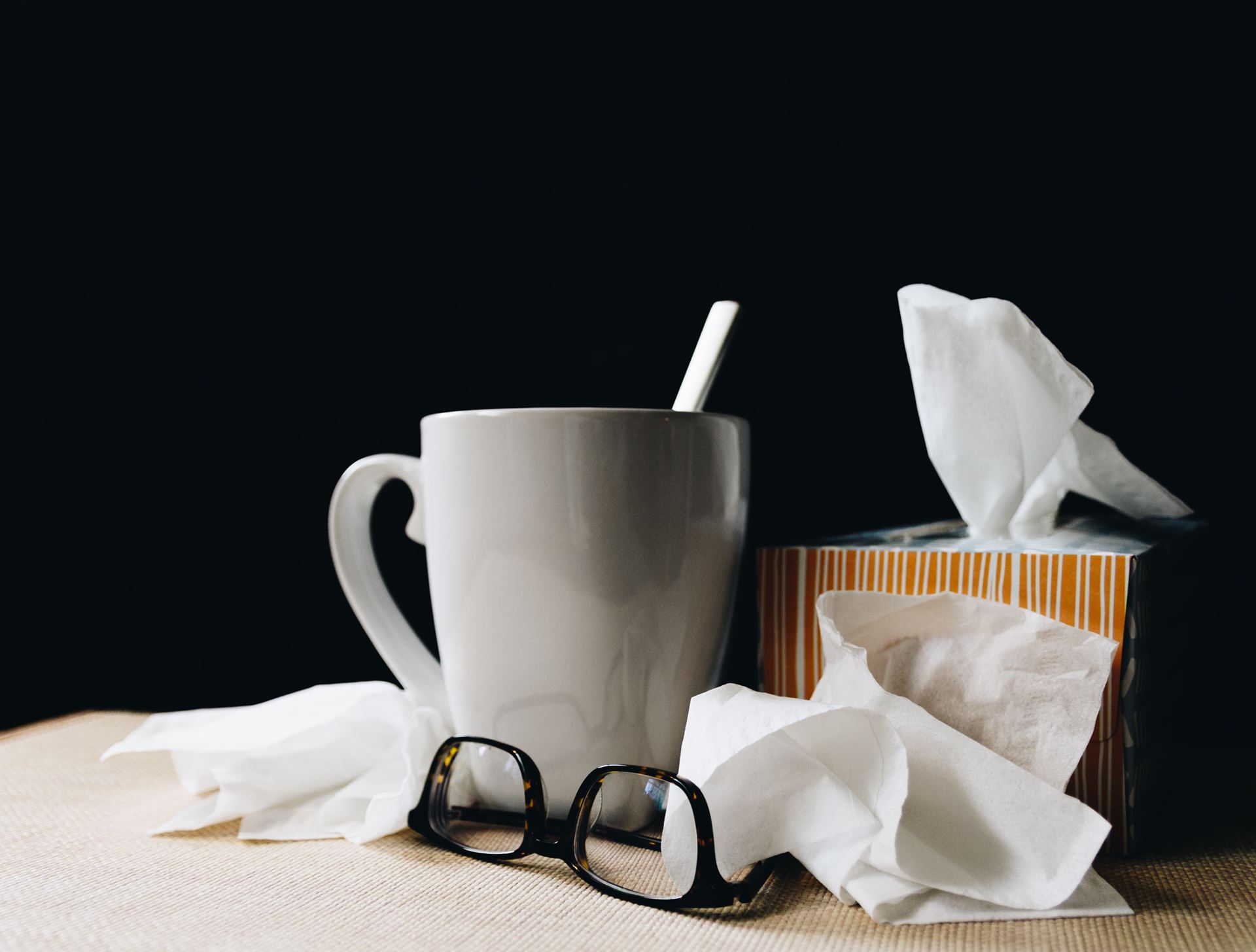 a hot drink in a mug, a box of tissues and a pair of spectacles on a table