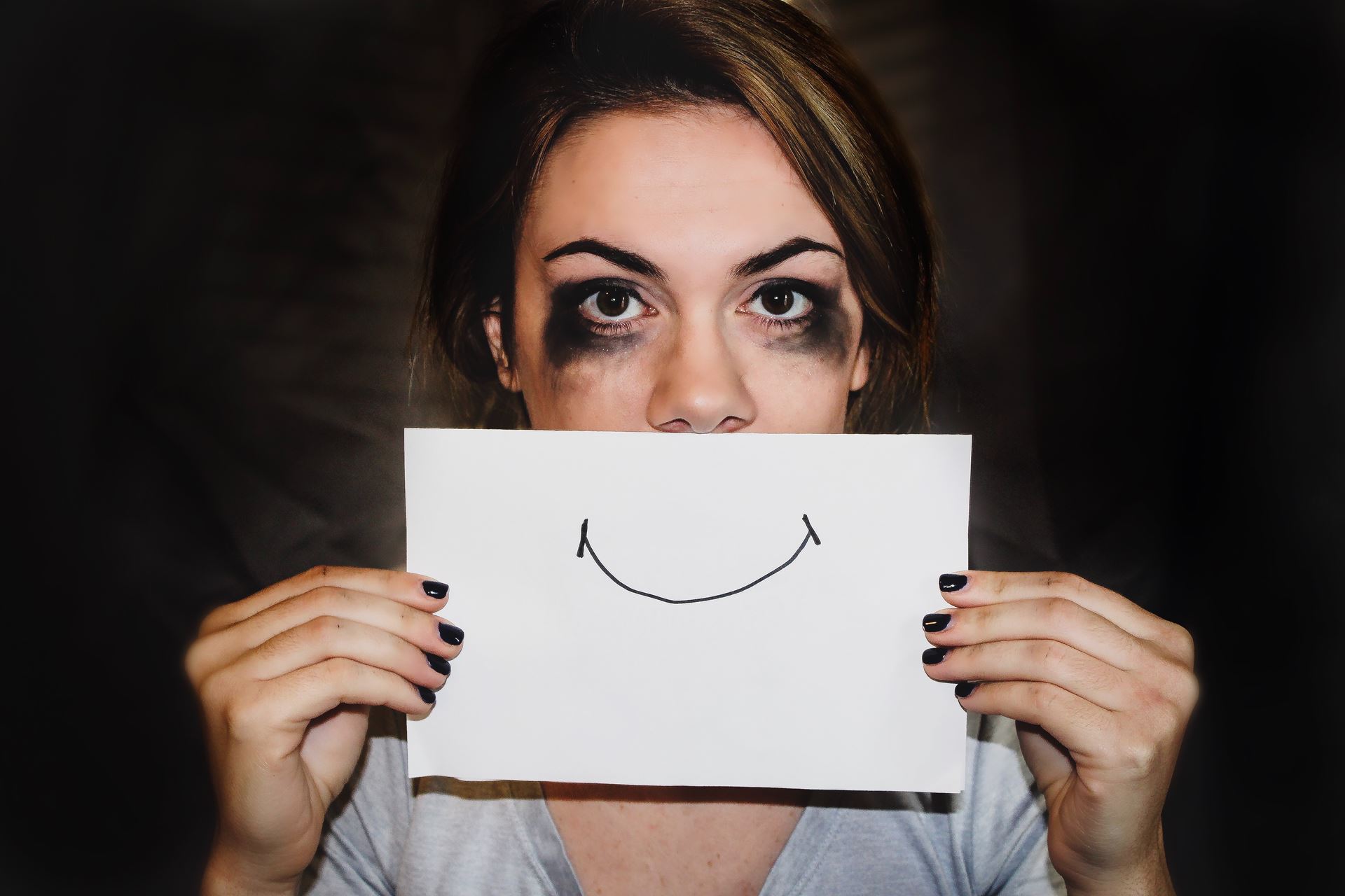 a woman with smudged mascara holding a picture of a smile in from of her face